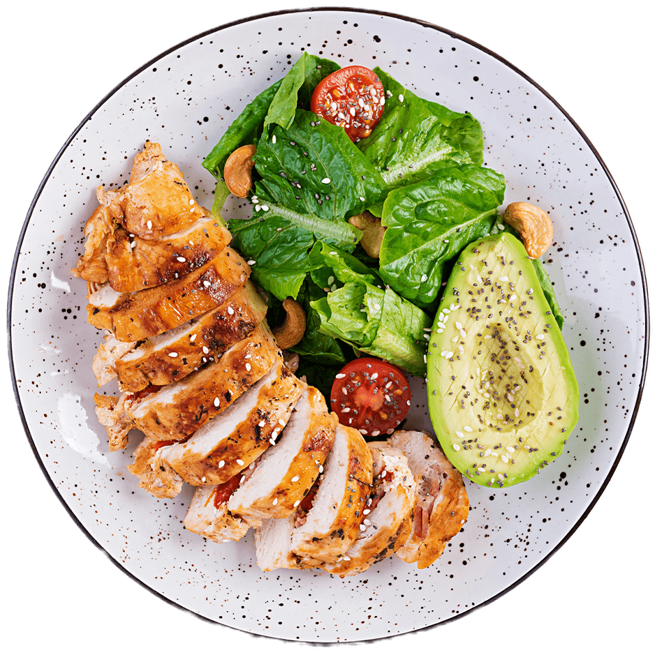 Pechuga de pollo a la parrilla en rebanadas con ensalada de lechuga, tomate cherry, anacardos y aguacate con semillas de chía, servido en un plato blanco con motas negras.