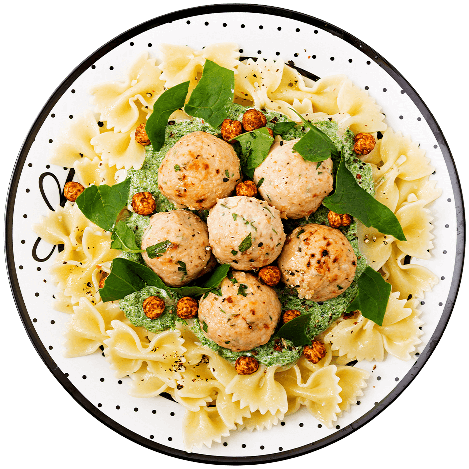 Plato de pasta farfalle con albóndigas de pollo, salsa de espinaca y garbanzos crujientes, servido en un plato blanco con detalles en negro.